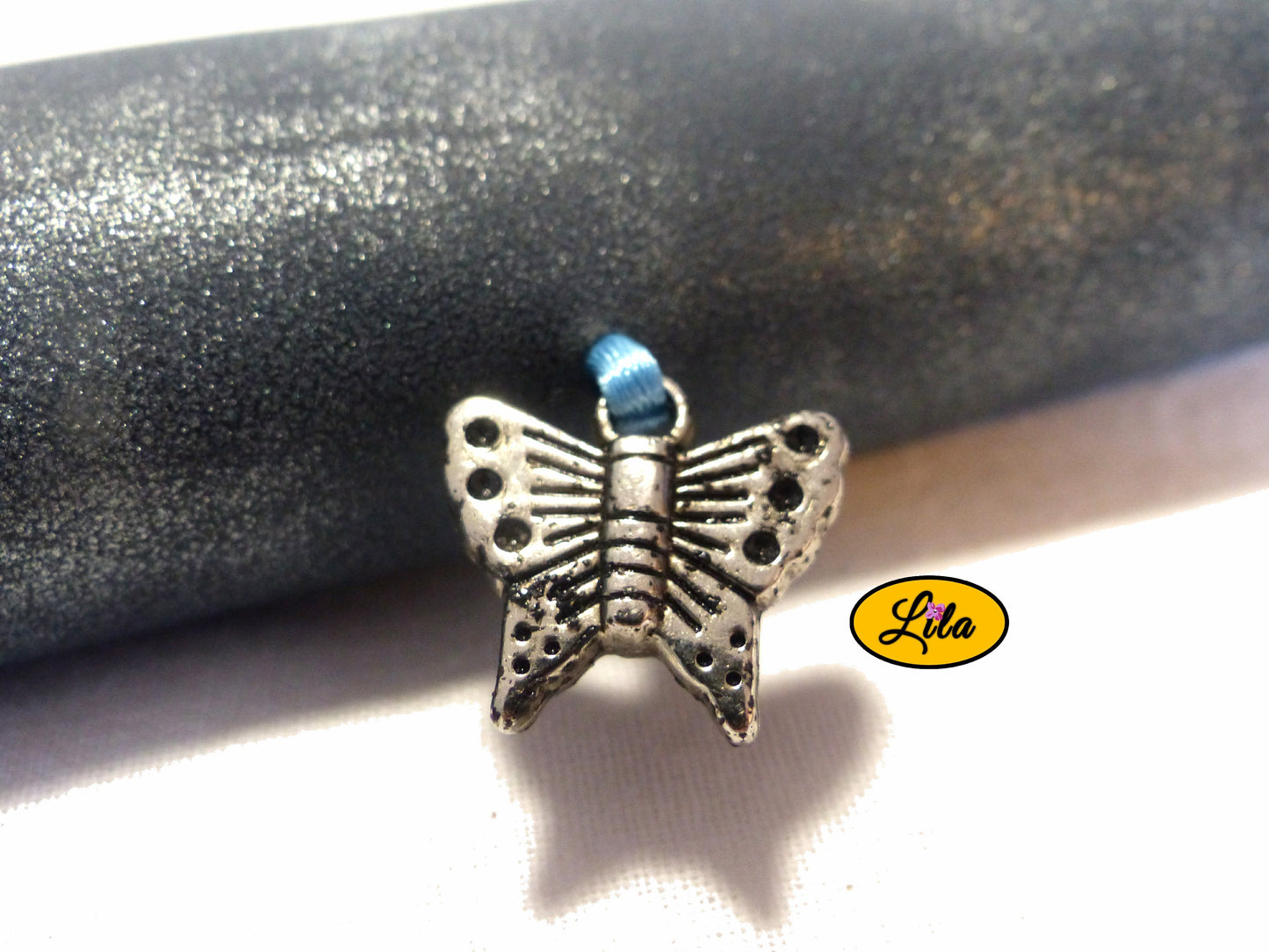 Zoom sur le pendentif papillon argenté décoratif de l’étui à lunettes en simili bleu argenté détail brillant et féminin