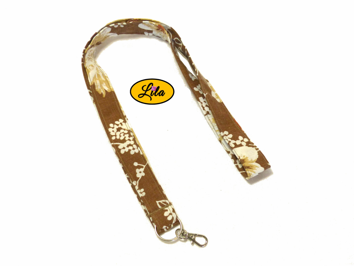 Porte-badge en tissu brun à petites fleurs blanches légèrement replié en deux sur fond blanc avec mousqueton métallique style pratique et artisanal