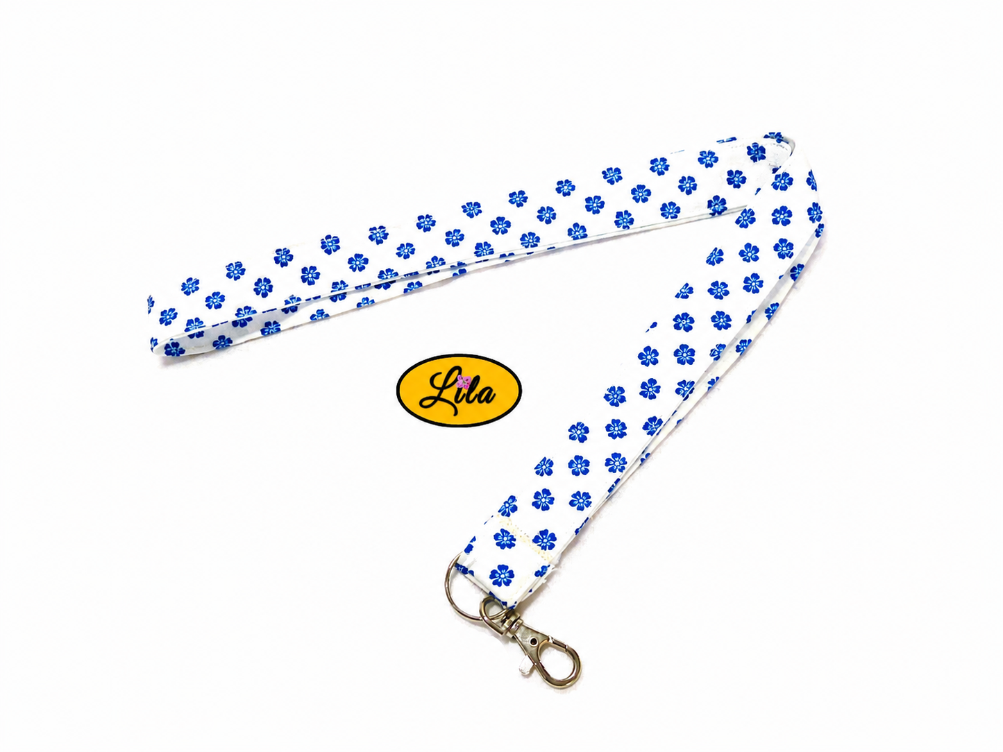 Porte-badge en tissu blanc à petites fleurs bleues légèrement replié en deux sur fond blanc avec mousqueton métallique style pratique et féminin