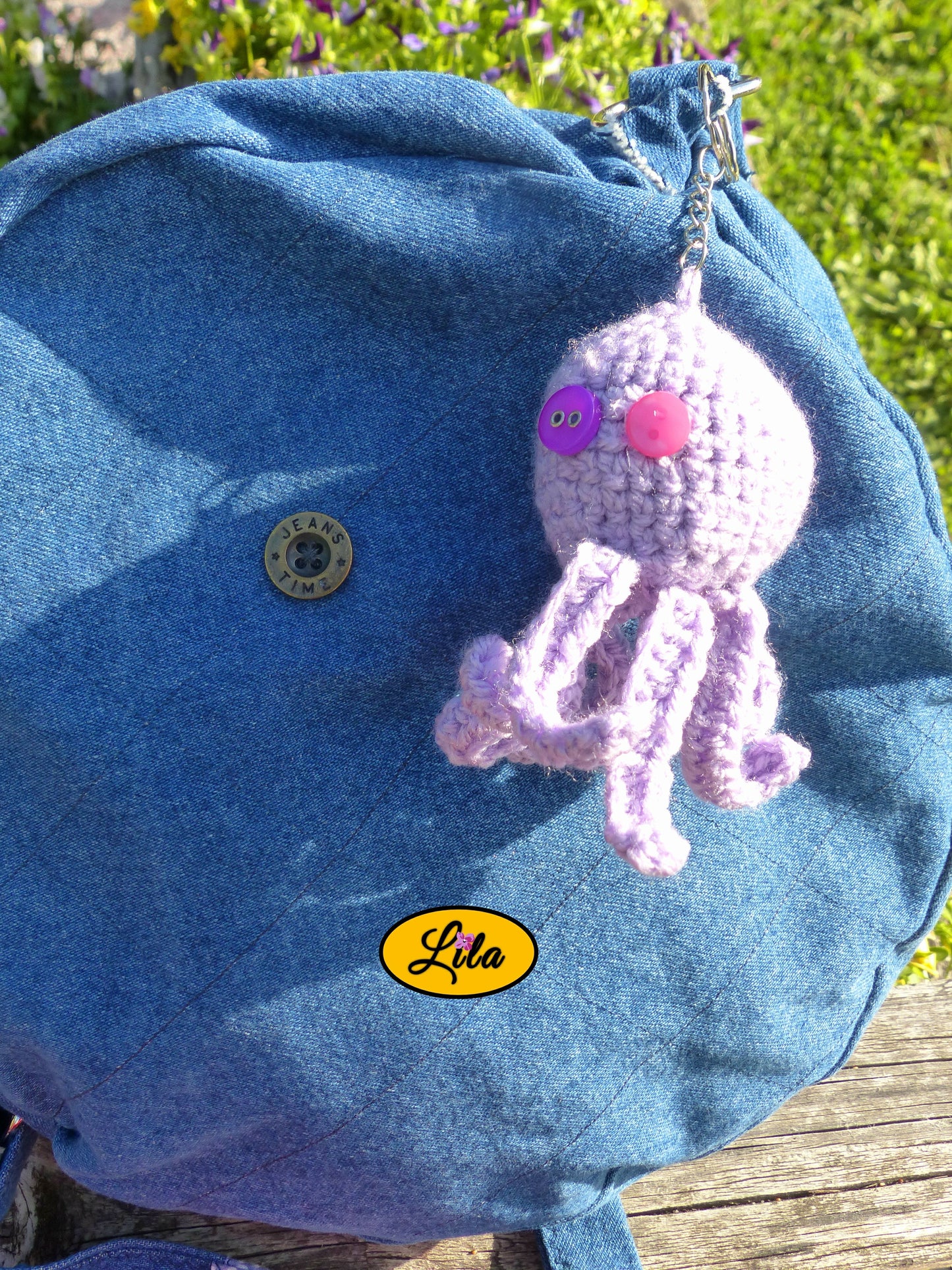 Porte-clé Poulpy pieuvre amigurumi mauve clair réalisée au crochet avec yeux en boutons mauve et rose accroché à un sac style bohème et artisanal