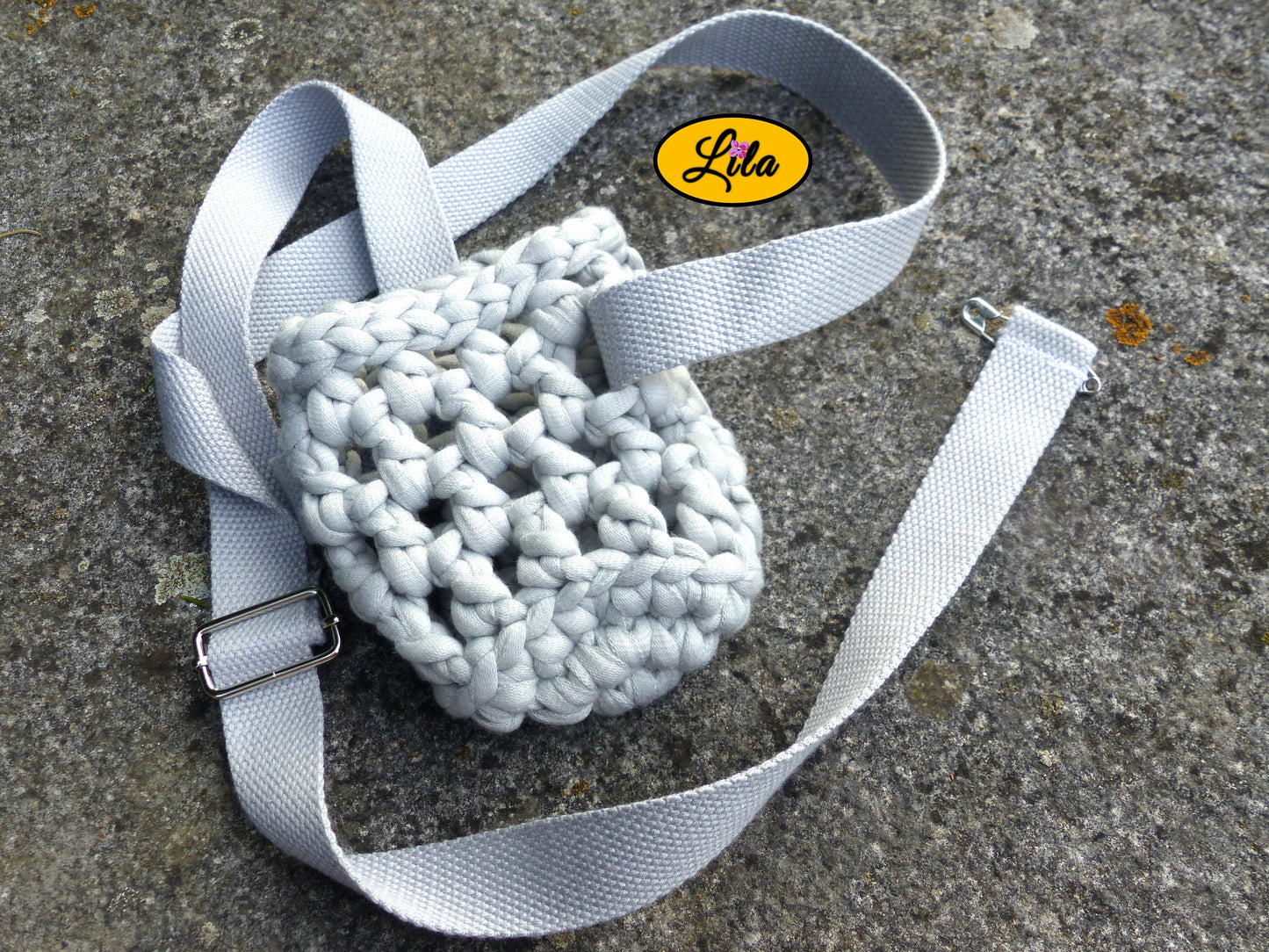 Porte-gobelet crocheté gris vu de haut à plat sur une pierre avec sangle grise autour style minimaliste et artisanal