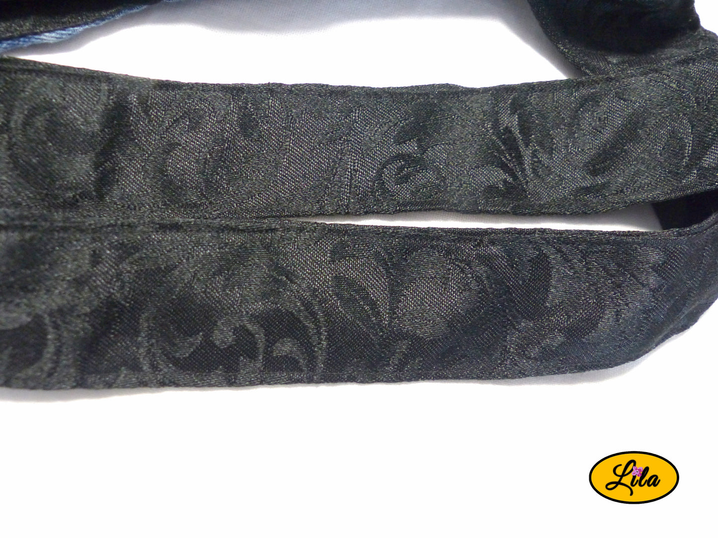 Zoom sur les anses noires à motifs floraux d’un sac patchwork en jeans recyclés sur fond blanc style original et artisanal