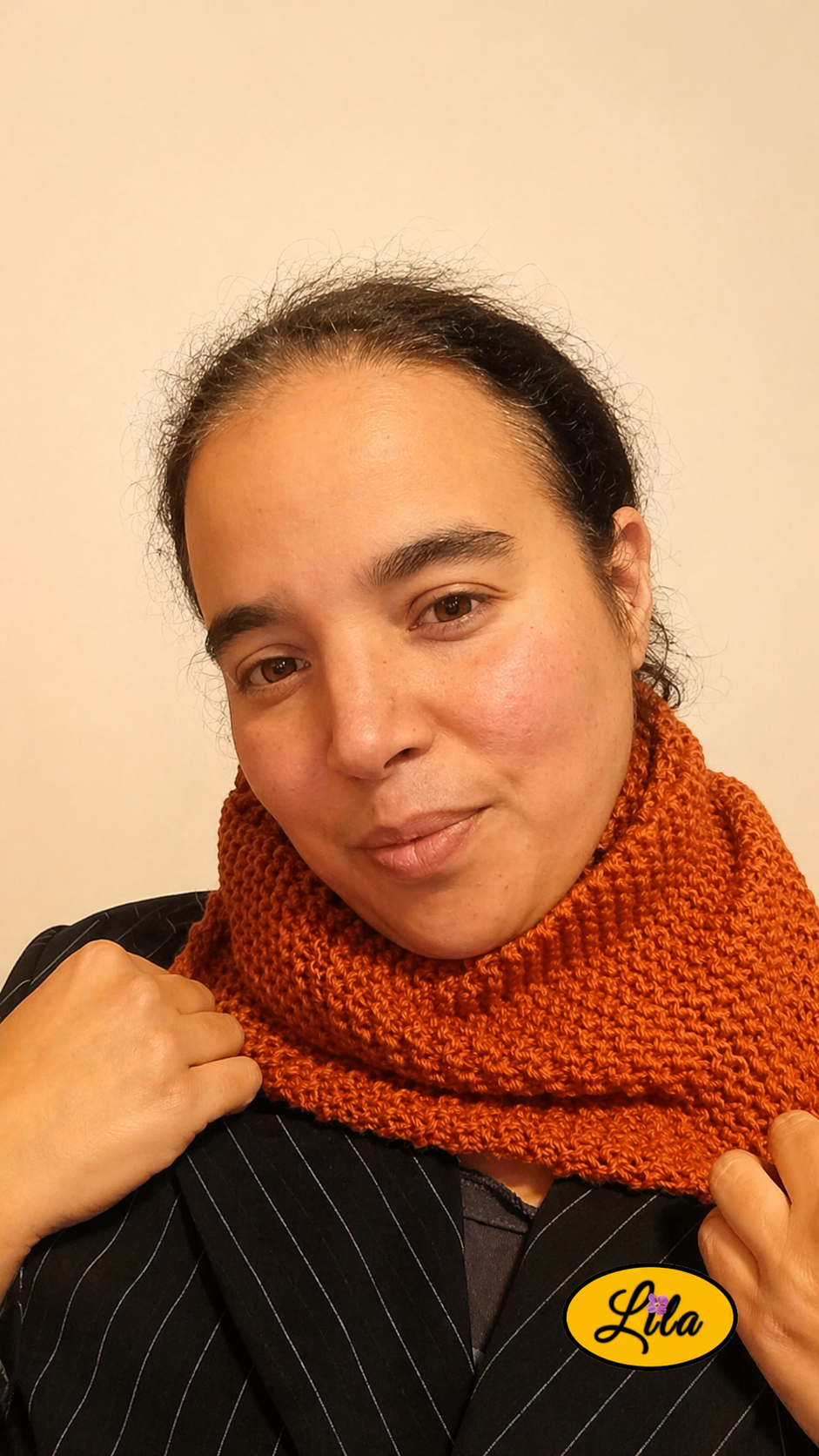 Snood en laine couleur rouille porté de face tête légèrement inclinée vers la droite avec les deux mains tenant le snood
