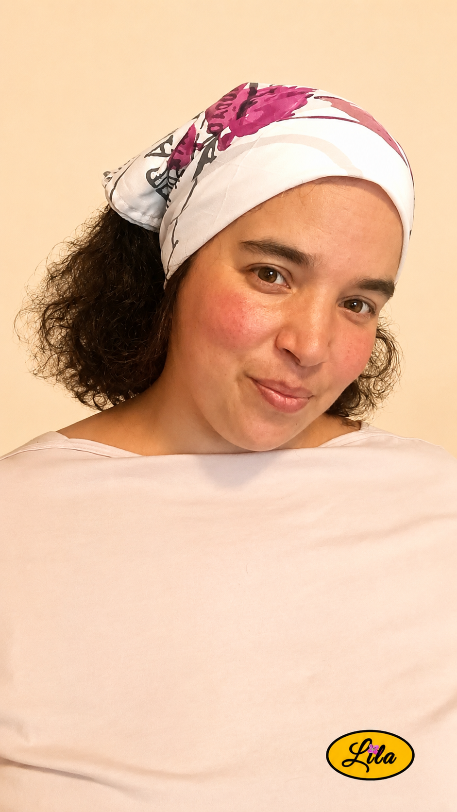 Bandana blanc à motifs de fleurs roses et inscriptions grises avec cachet Nature porté dans les cheveux par une femme de profil droit aux cheveux lâchés sur fond crème style bohème et romantique