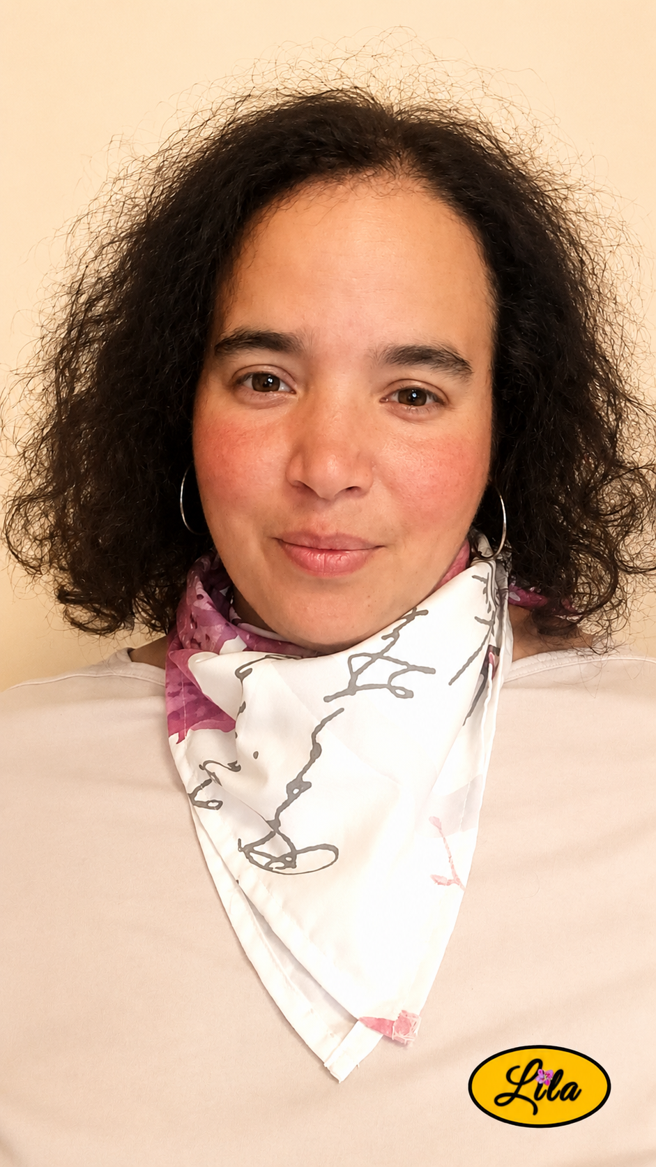 Bandana blanc à motifs floraux roses et inscriptions grises avec cachet Nature porté autour du cou par une femme de face aux cheveux détachés style romantique et tendance