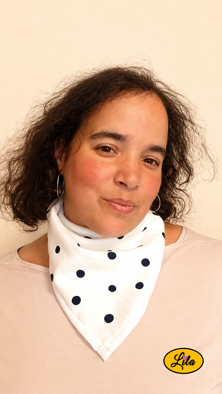 Bandana blanc à pois marine porté autour du cou par une femme aux cheveux lâchés avec la tête légèrement inclinée et un léger sourire style chic et intemporel