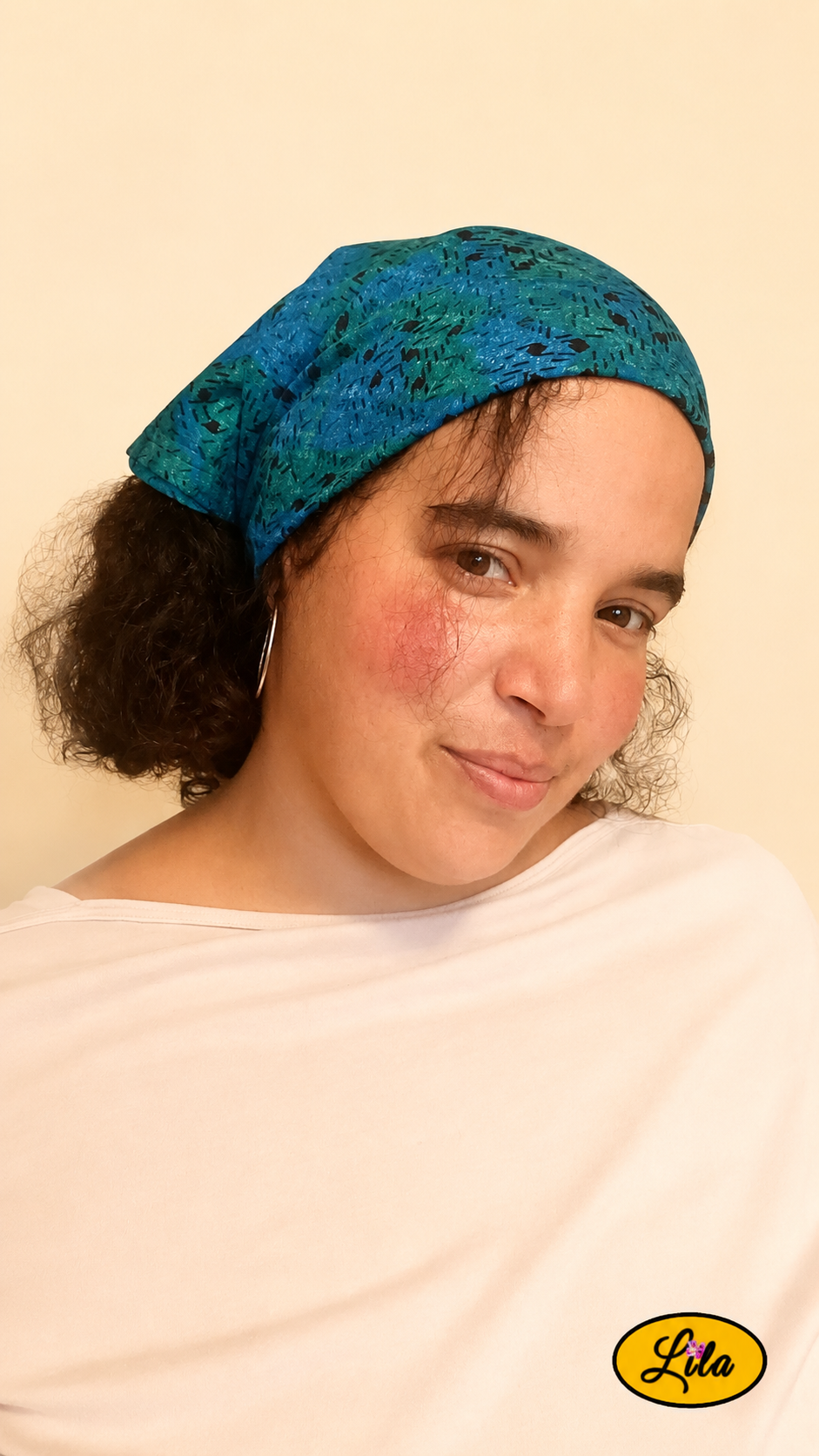 Bandana bleu et vert à motifs graphiques vintage porté dans les cheveux par une femme de profil droit avec les cheveux lâchés sous le bandana style graphique et artisanal