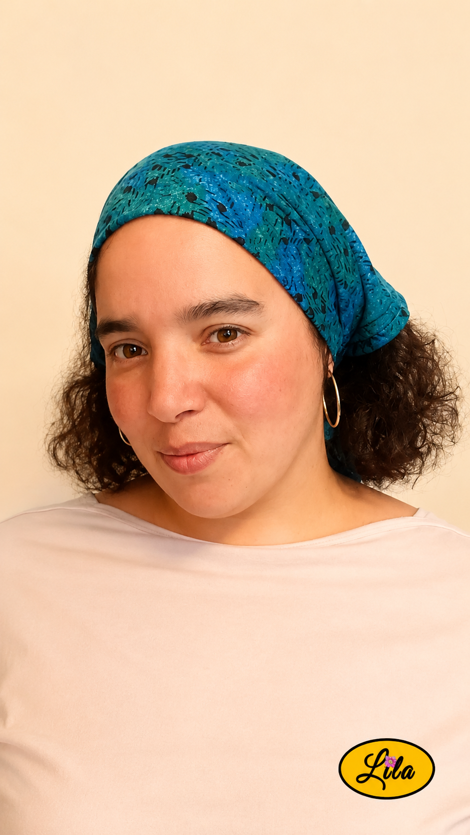 Bandana bleu et vert à motifs graphiques vintage porté dans les cheveux par une femme de profil gauche avec les cheveux lâchés sous le bandana style rétro et tendance