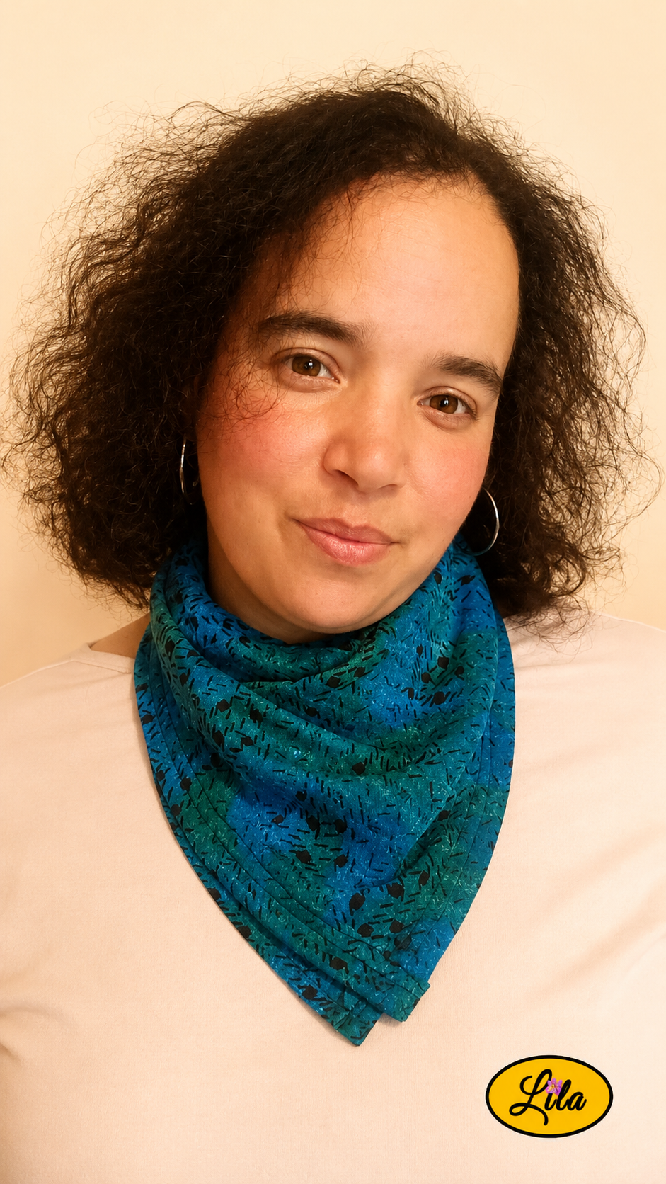 Bandana bleu et vert à motifs graphiques vintage porté autour du cou par une femme de face aux cheveux lâchés avec la tête légèrement inclinée et un léger sourire style rétro et élégant