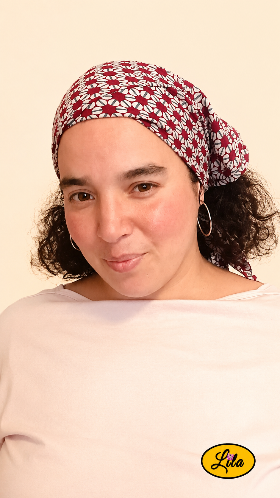 Bandana bordeaux à motifs géométriques vintage porté dans les cheveux par une femme la tête légèrement inclinée vers le bas, de profil gauche, avec les cheveux lâchés sous le bandana style rétro et élégant
