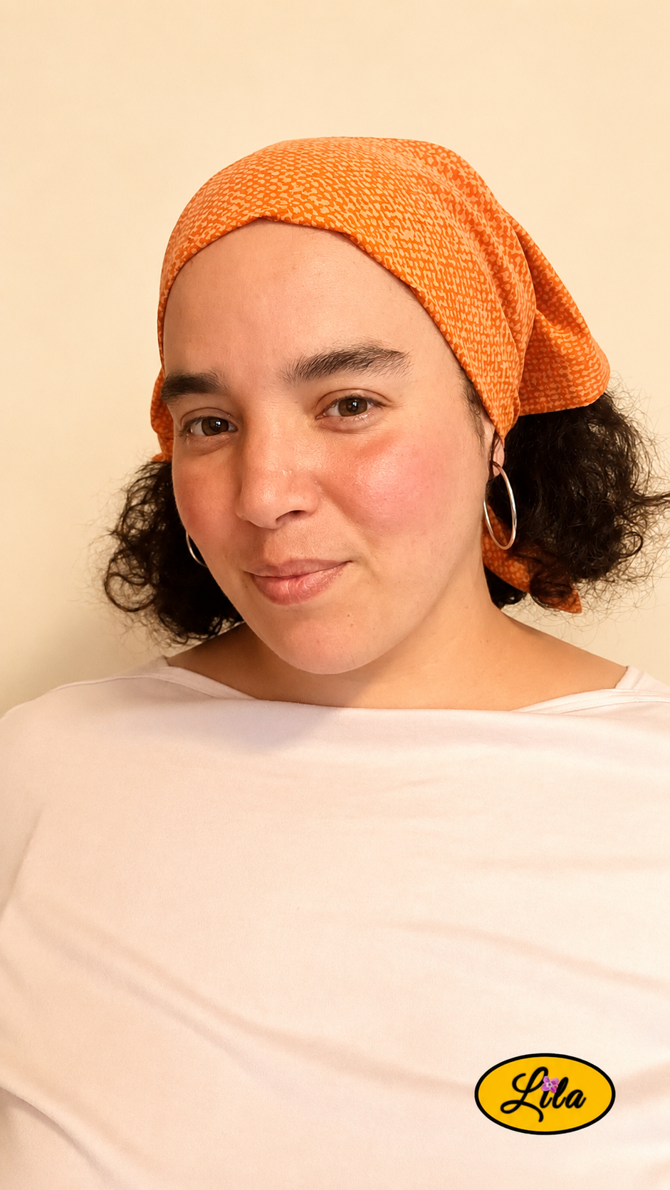 Bandana orange à motif texturé vintage porté dans les cheveux par une femme légèrement de profil gauche avec les cheveux lâchés sous le bandana style bohème et rétro
