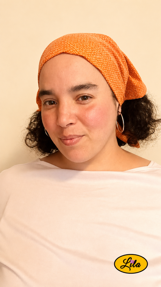 Bandana orange à motif texturé vintage porté dans les cheveux par une femme légèrement de profil gauche avec les cheveux lâchés sous le bandana style bohème et rétro
