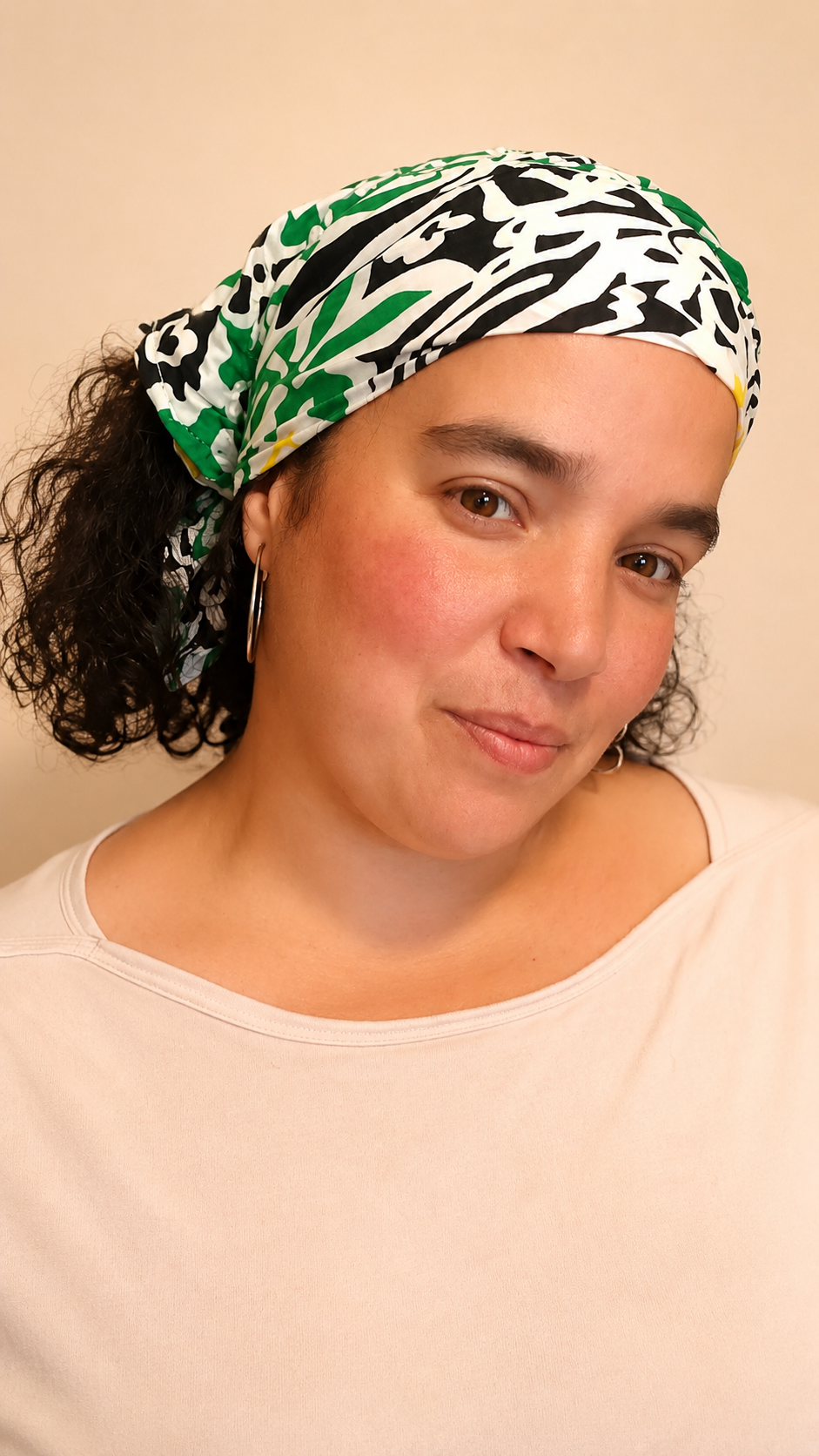Bandana vert et jaune à motifs floraux vintage porté dans les cheveux par une femme de profil droit avec les cheveux lâchés sous le bandana, photo rapprochée mettant en valeur le côté vert du tissu