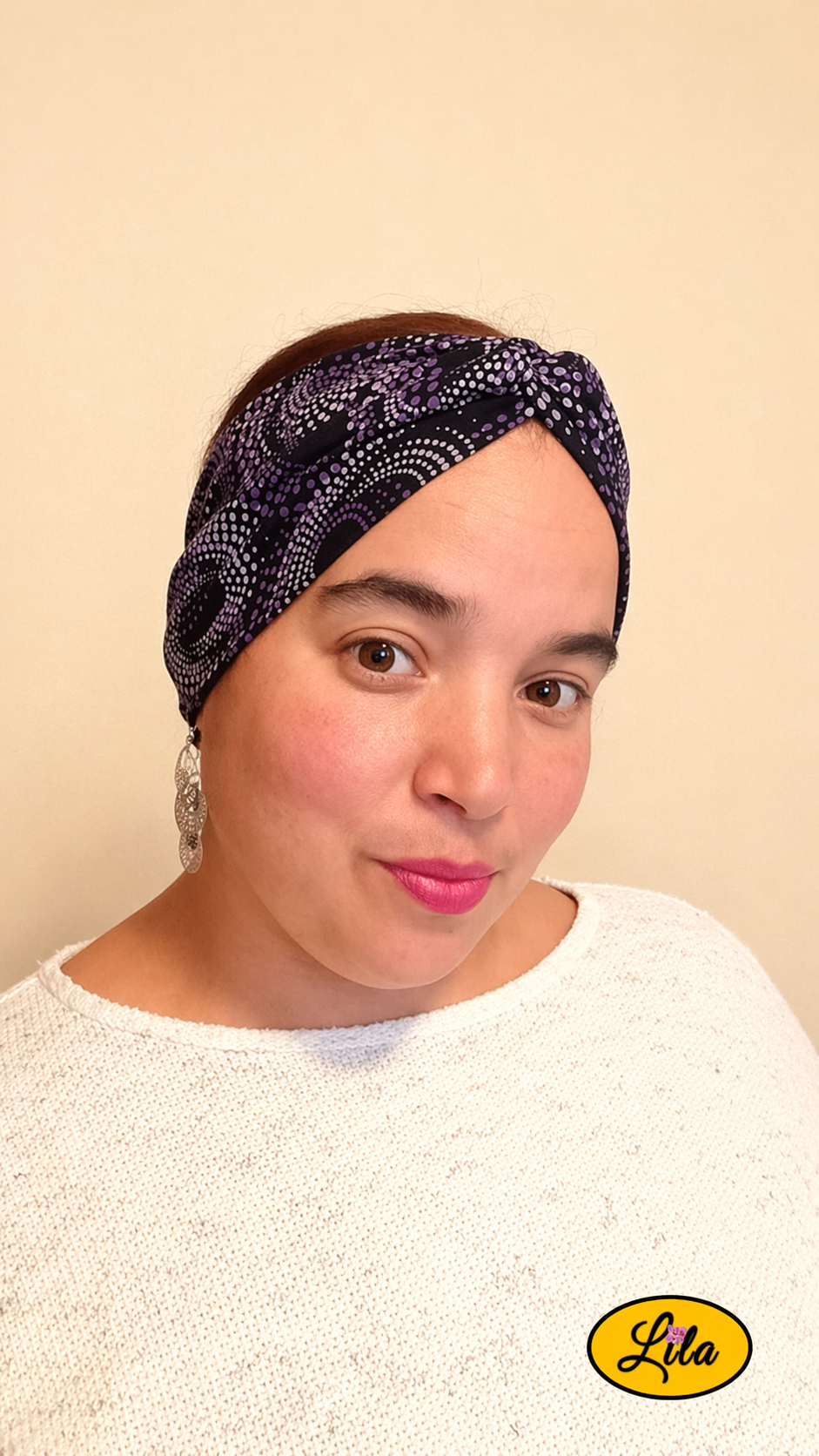 Bandeau en tissu noir à pois mauve porté de face tête légèrement inclinée vers la droite avec noeud au-dessus