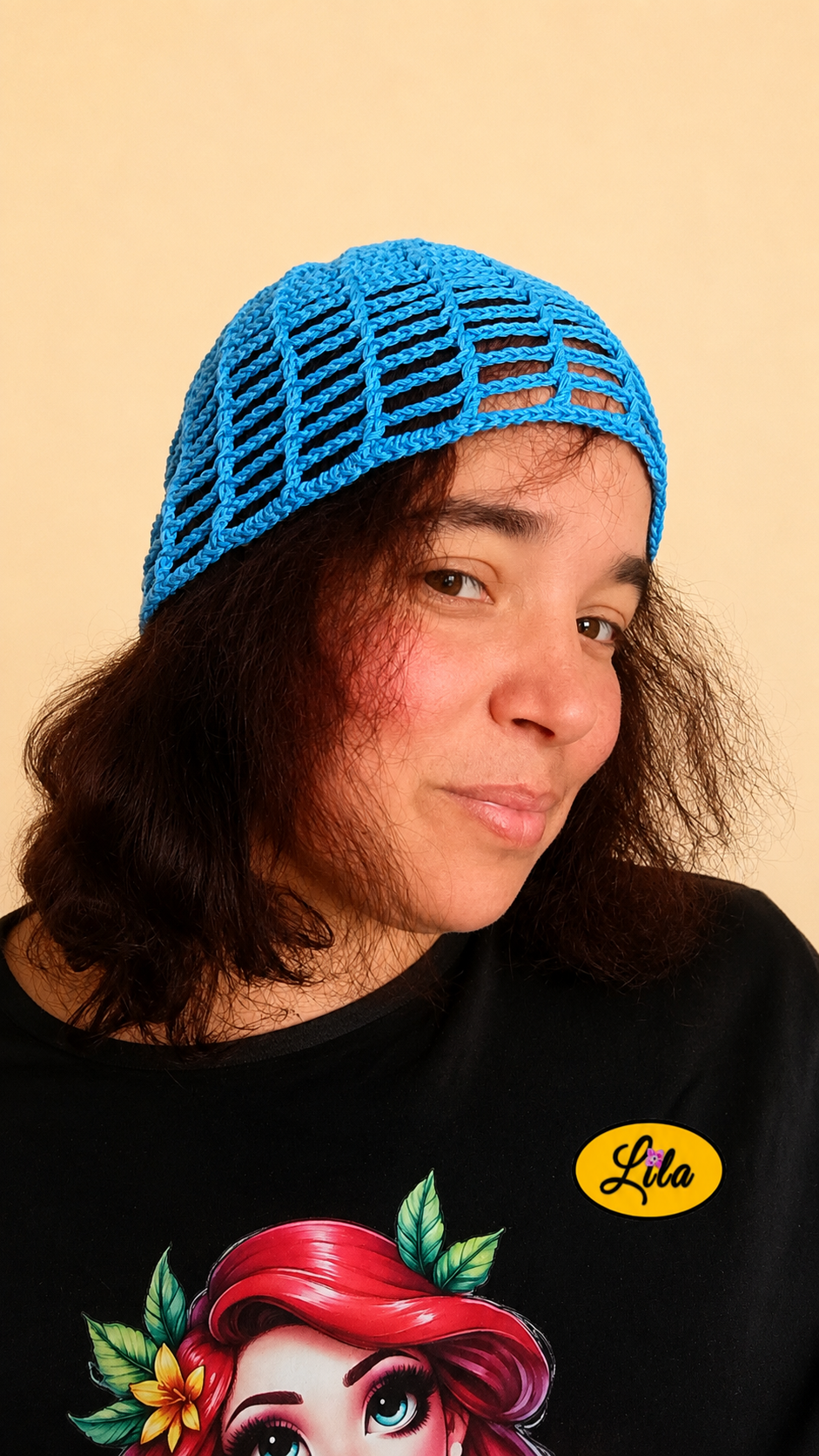 Bonnet d'été en crochet ajouré bleu porté par un mannequin légèrement de profil droit avec les cheveux lâchés, regard de face et léger sourire, mettant en valeur son style bohème et son crochet fait main