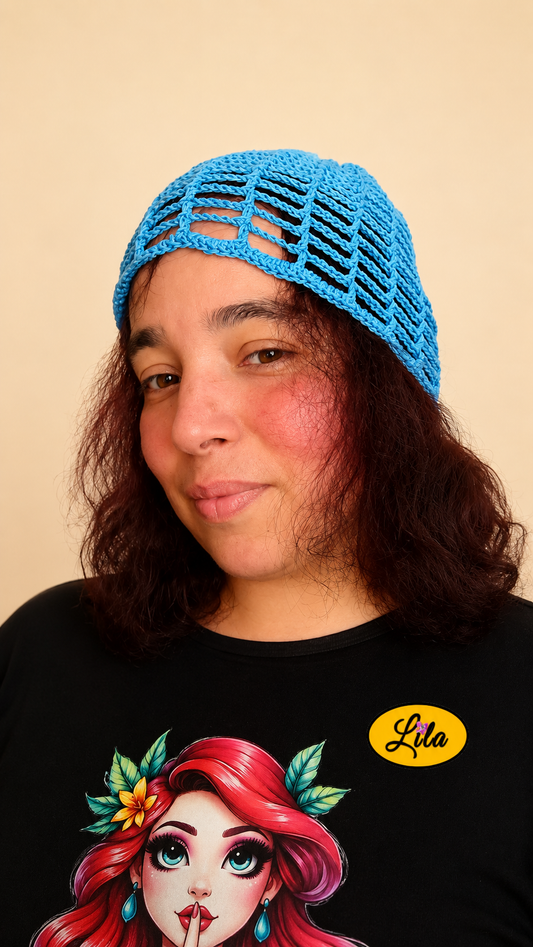 Bonnet d'été en crochet ajouré bleu porté par un mannequin légèrement de profil gauche avec les cheveux lâchés, regard de face et léger sourire, mettant en valeur sa légèreté, son motif ajouré et sa confection artisanale