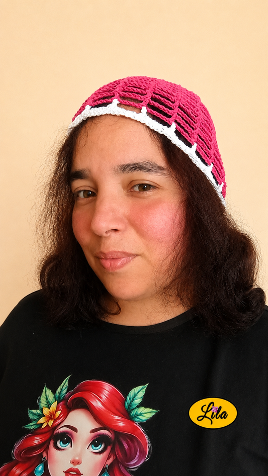 Bonnet d'été en crochet ajouré rose avec bande blanche porté par un mannequin de profil gauche avec les cheveux lâchés mettant en valeur sa maille ajourée, son contraste de couleurs et sa confection artisanale