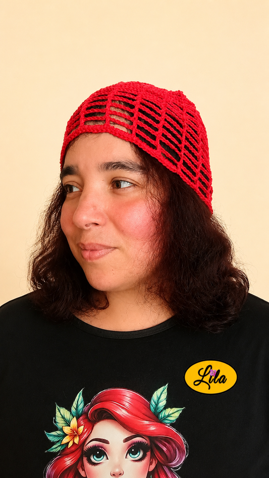 Bonnet d'été en crochet ajouré rouge porté par un mannequin de profil gauche avec les cheveux lâchés et le regard tourné vers la gauche mettant en valeur sa maille ajourée, sa coupe confortable et sa confection artisanale