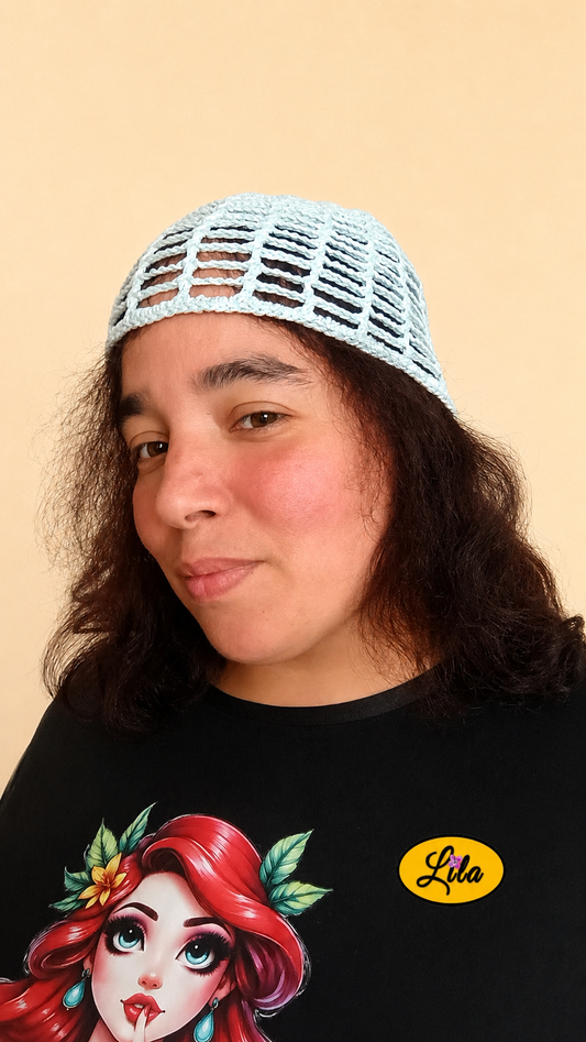 Bonnet d'été en crochet ajouré vert menthe porté par un mannequin de profil gauche avec les cheveux lâchés et le regard dirigé vers l'avant mettant en valeur sa maille ajourée, sa coupe confortable et sa confection artisanale