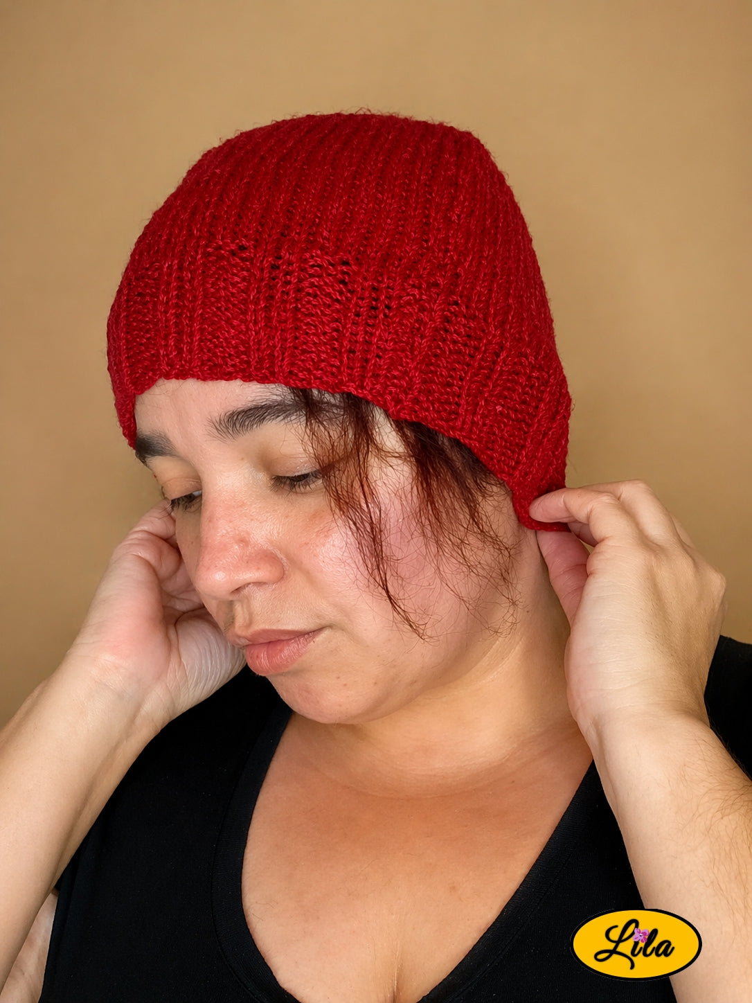 Bonnet en laine rouge porté profil gauche regard vers le bas avec main ajustant le bonnet à l’arrière
