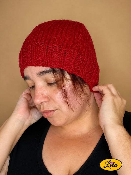 Bonnet en laine rouge porté profil gauche regard vers le bas avec main ajustant le bonnet à l’arrière