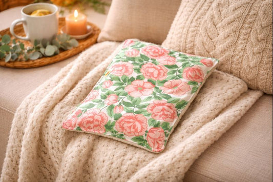 Bouillotte carrée fleurie réalisée dans un ancien drap de lit recyclé et remplie de noyaux de cerise posée sur un fauteuil avec plaid oreiller et bougie allumée ambiance cocooning et chaleureuse