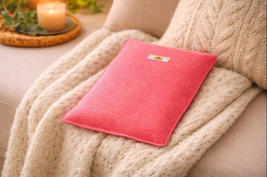 Bouillotte simple rouge et orange réalisée dans d’anciens draps de lit recyclés et remplie de noyaux de cerise posée sur un fauteuil avec plaid oreiller et bougie allumée ambiance cocooning et chaleureuse