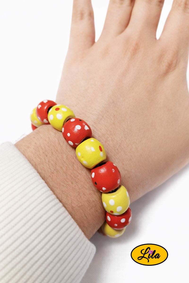 Bracelet en perles de bois jaunes et rouges avec pois blancs porté au poignet style coloré