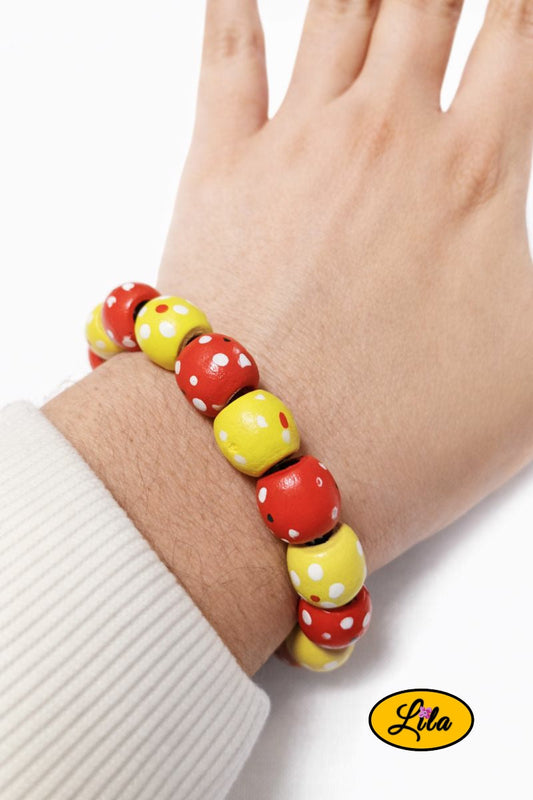 Bracelet en perles de bois jaunes et rouges avec pois blancs porté au poignet style coloré