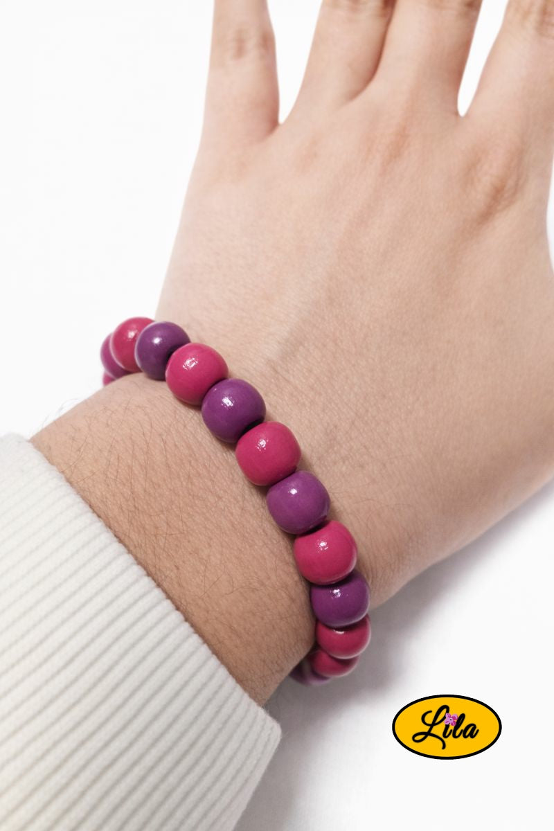 Bracelet en perles rondes en bois rose et mauve porté au poignet style naturel