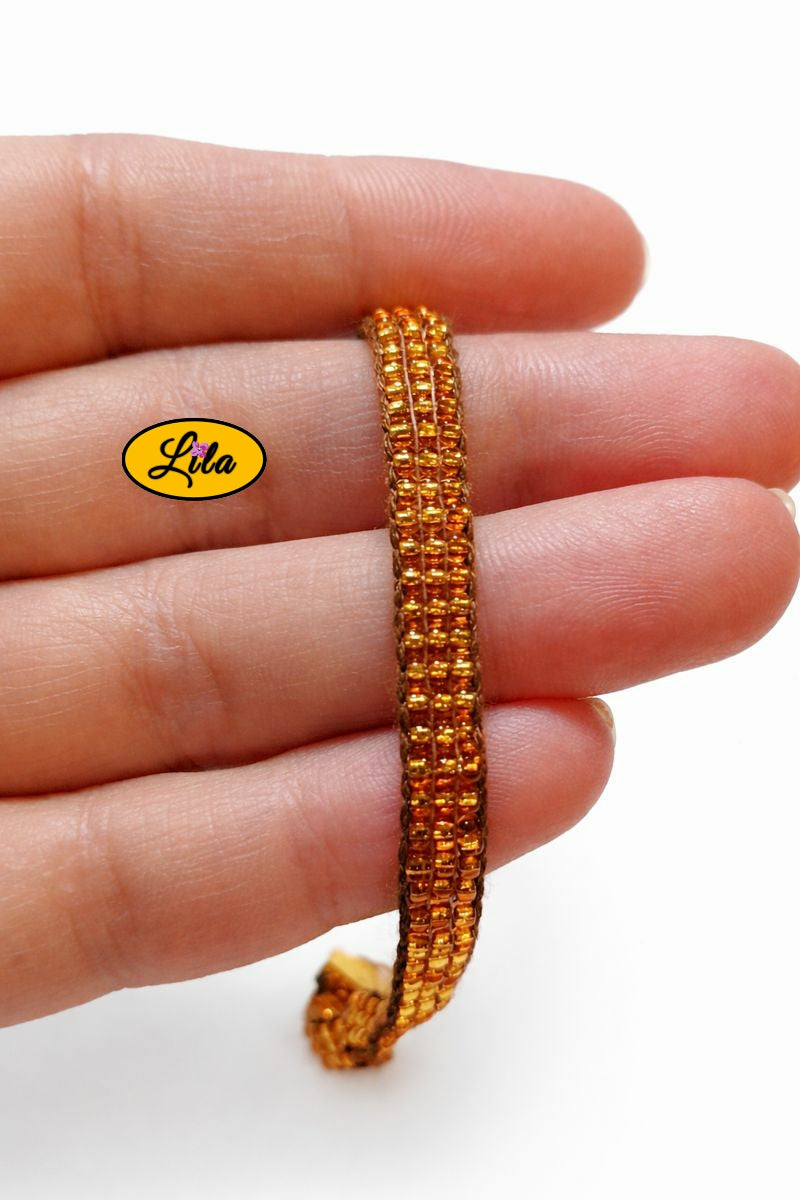 Détail tissage bracelet en perles de rocailles dorées tenu en main