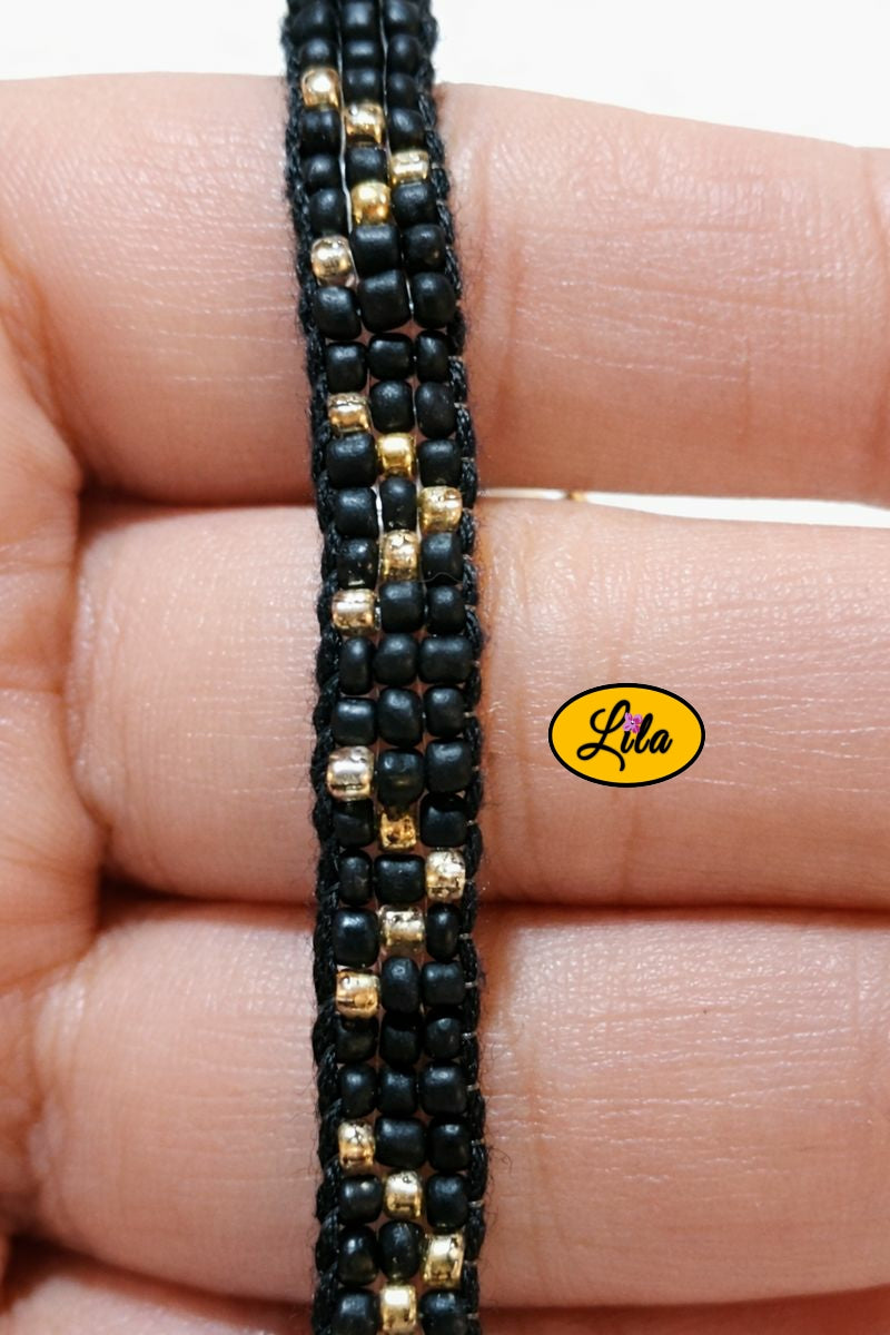 Détail tissage bracelet en perles de rocailles noires et dorées tenu en main