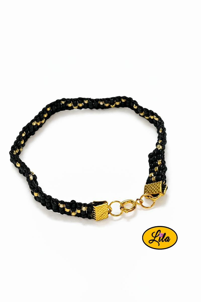 Bracelet tissé perles de rocailles noires et dorées vue de dessus sur fond blanc