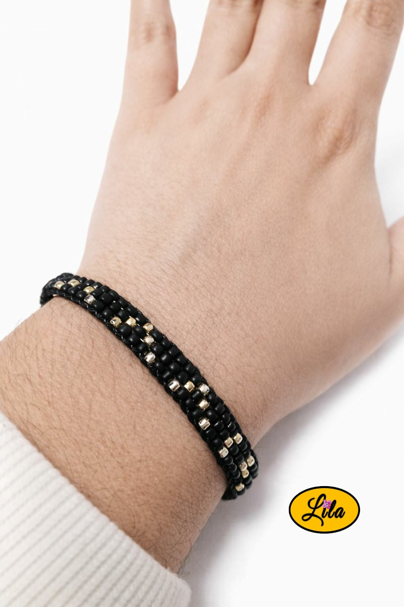 Bracelet tissé en perles de rocailles noires avec touches dorées porté au poignet style élégant