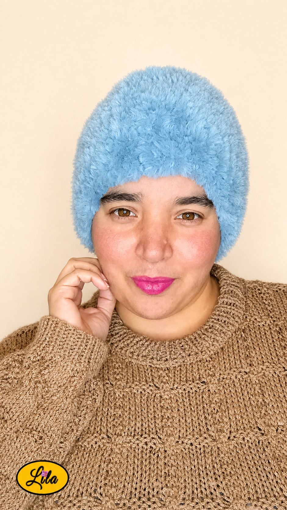 Cache-cou tricoté main bleu effet fausse fourrure porté sur la tête par une femme avec pull brun sur fond crème tenant le cache-cou avec la main droite style cocooning et élégant