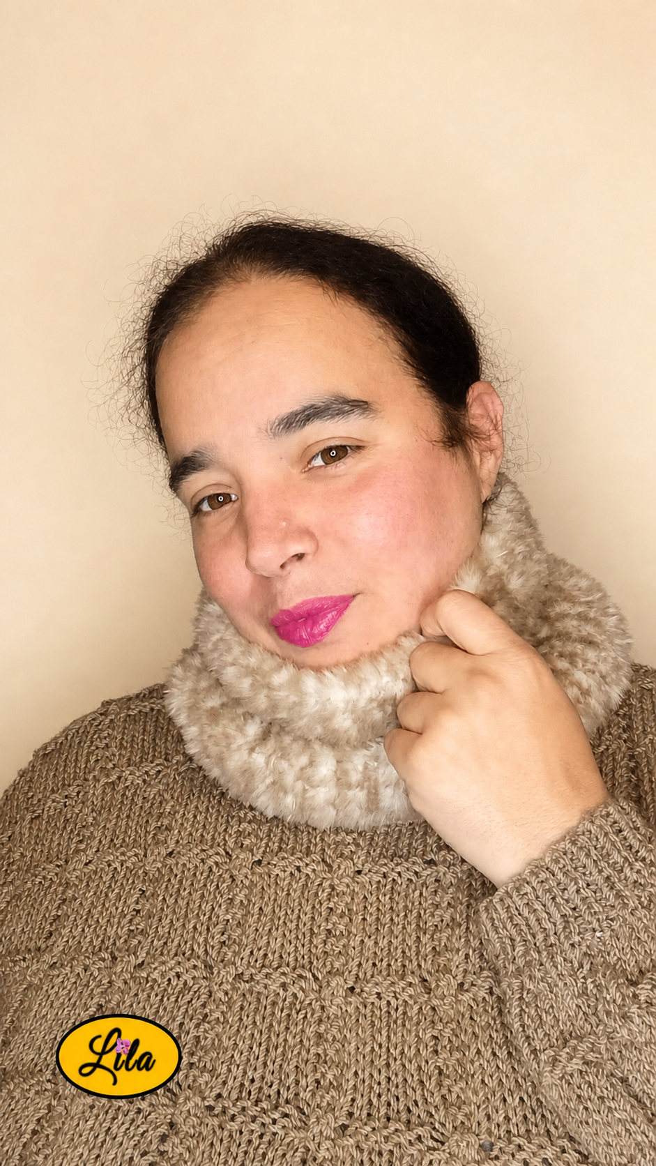 Cache-cou tricoté main brun chamarré effet fausse fourrure porté dans le cou par une femme avec pull brun sur fond crème main gauche tenant le haut du cache-cou style doux et hivernal