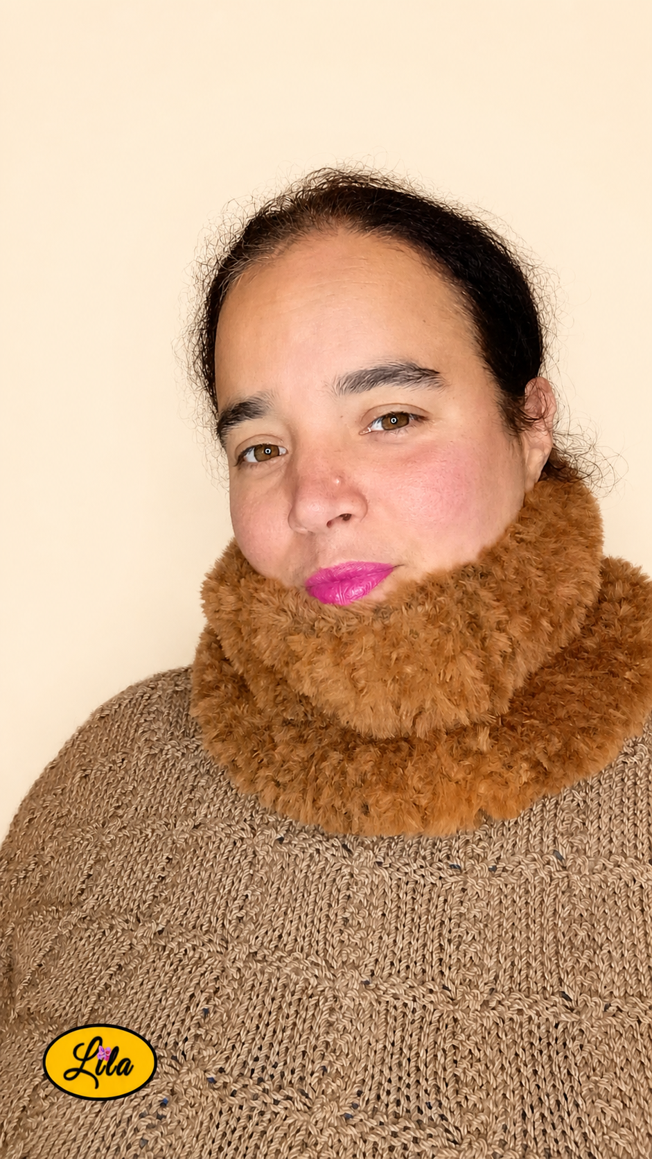 Cache-cou tricoté main brun effet fausse fourrure porté dans le cou par une femme légèrement de profil gauche avec pull brun sur fond crème style doux et tendance