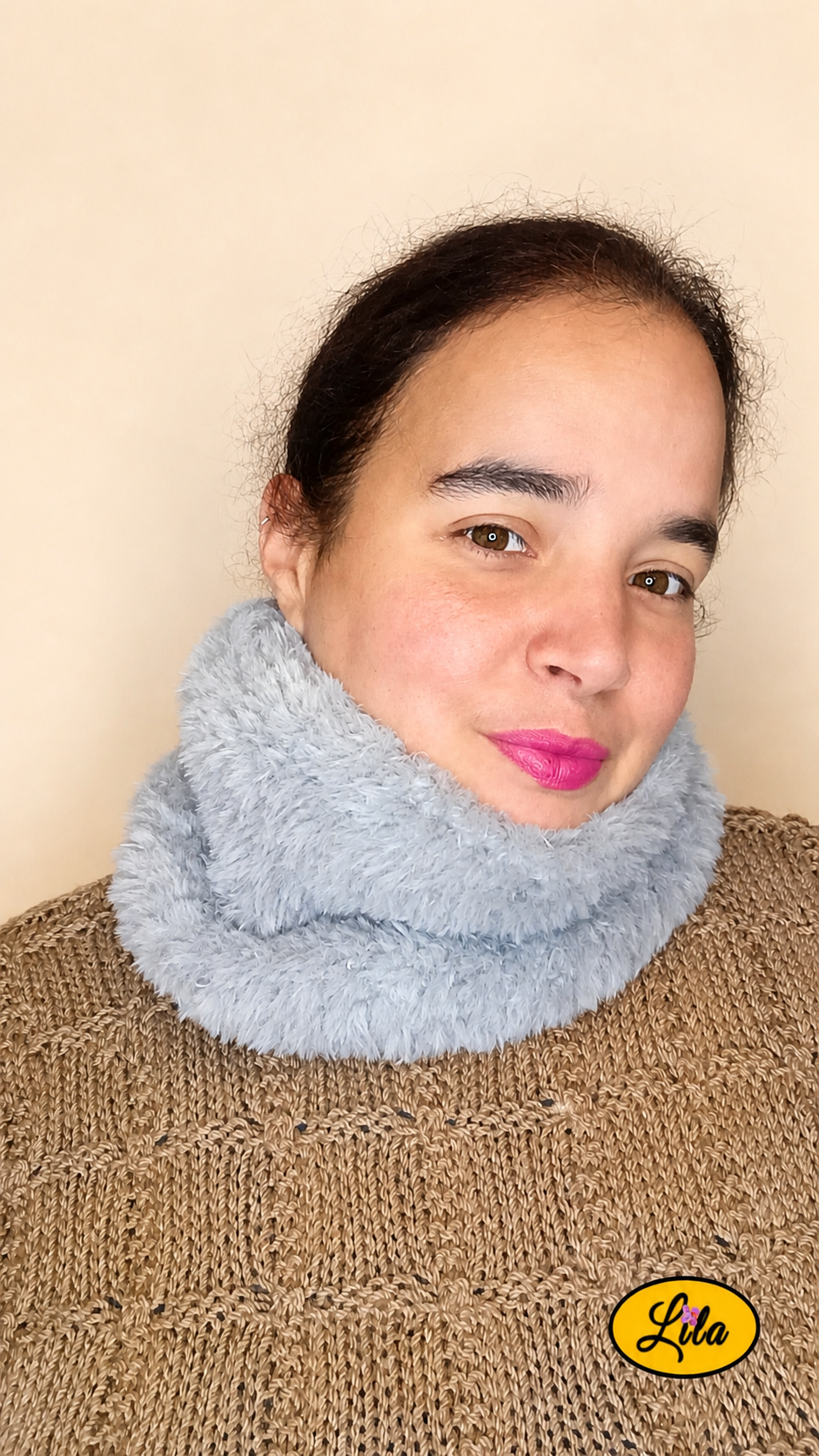 Cache-cou tricoté main gris effet fausse fourrure porté par une femme avec pull brun sur fond crème vue de face tête légèrement inclinée à gauche style doux et cocooning