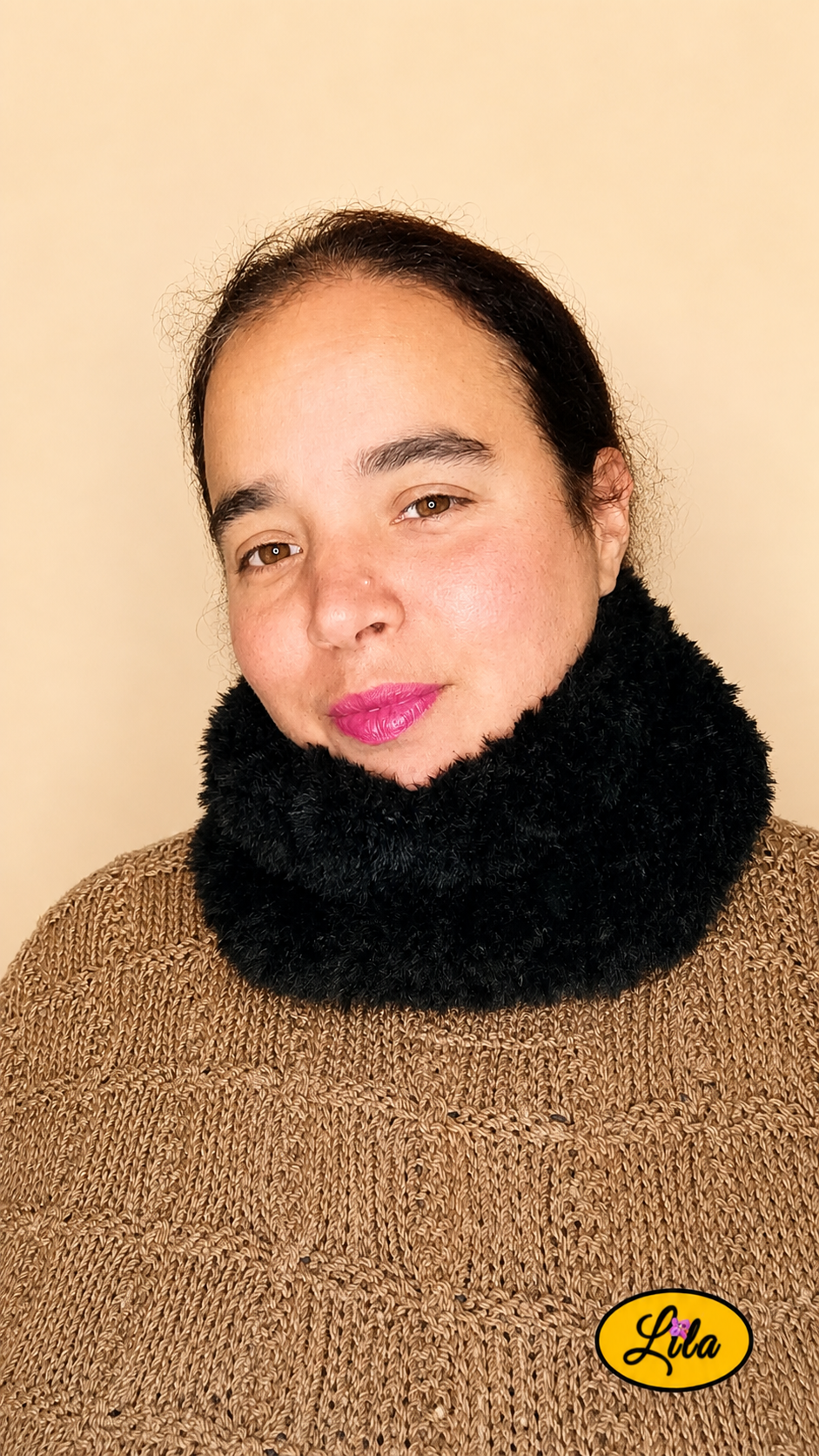 Cache-cou tricoté main noir effet fausse fourrure porté dans le cou par une femme avec pull brun sur fond crème tête légèrement tournée vers la droite style doux et tendance