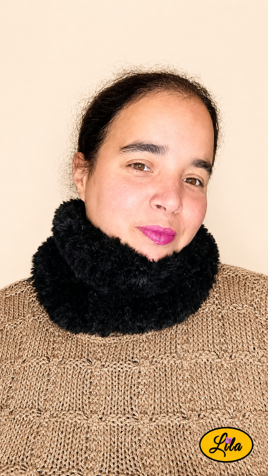 Cache-cou tricoté main noir effet fausse fourrure porté dans le cou par une femme avec pull brun sur fond crème tête légèrement tournée vers la gauche style élégant et hivernal