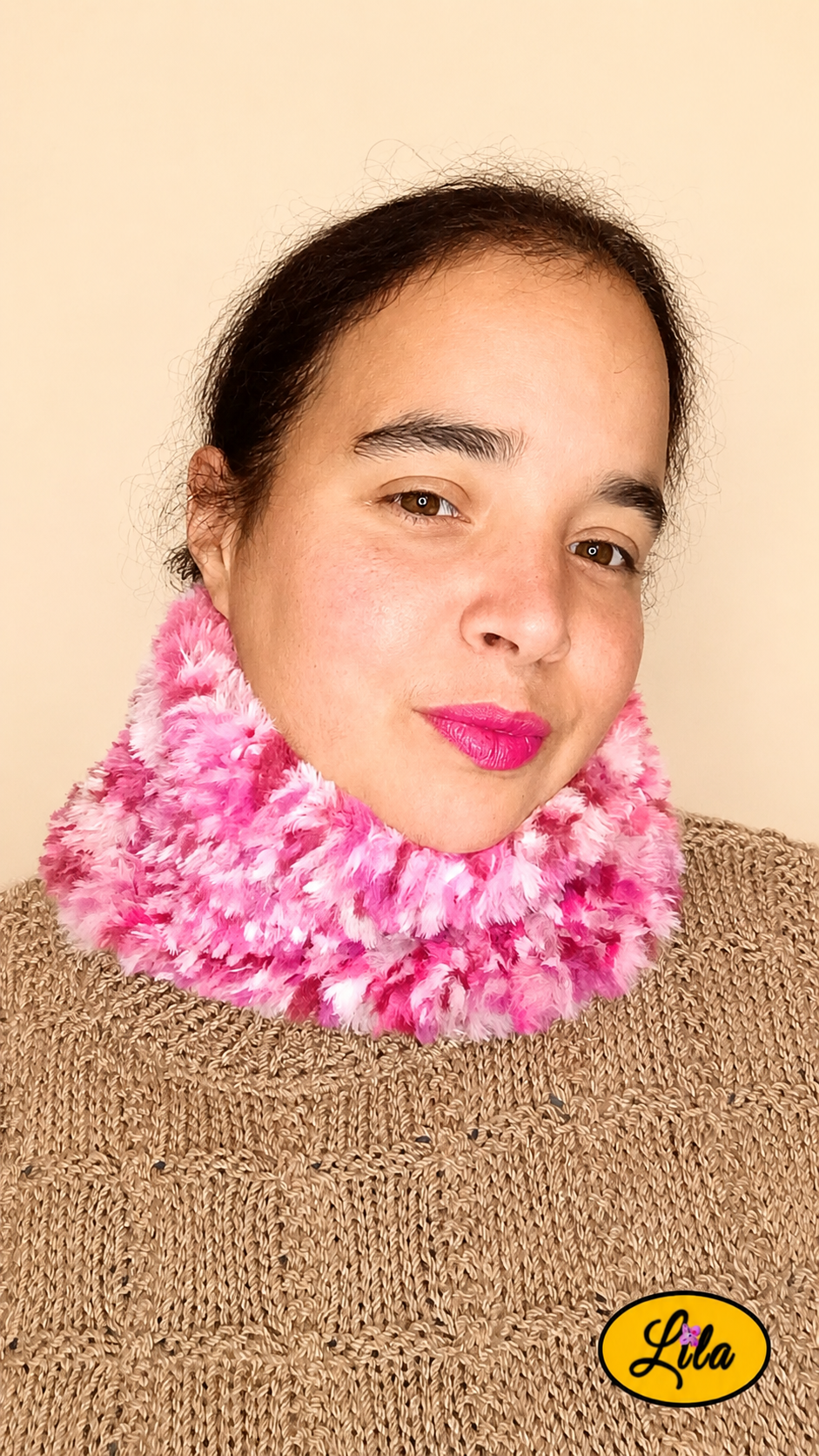 Cache-cou tricoté main rose chamarré effet fausse fourrure porté par une femme avec pull brun sur fond crème tête tournée vers la gauche style doux et élégant
