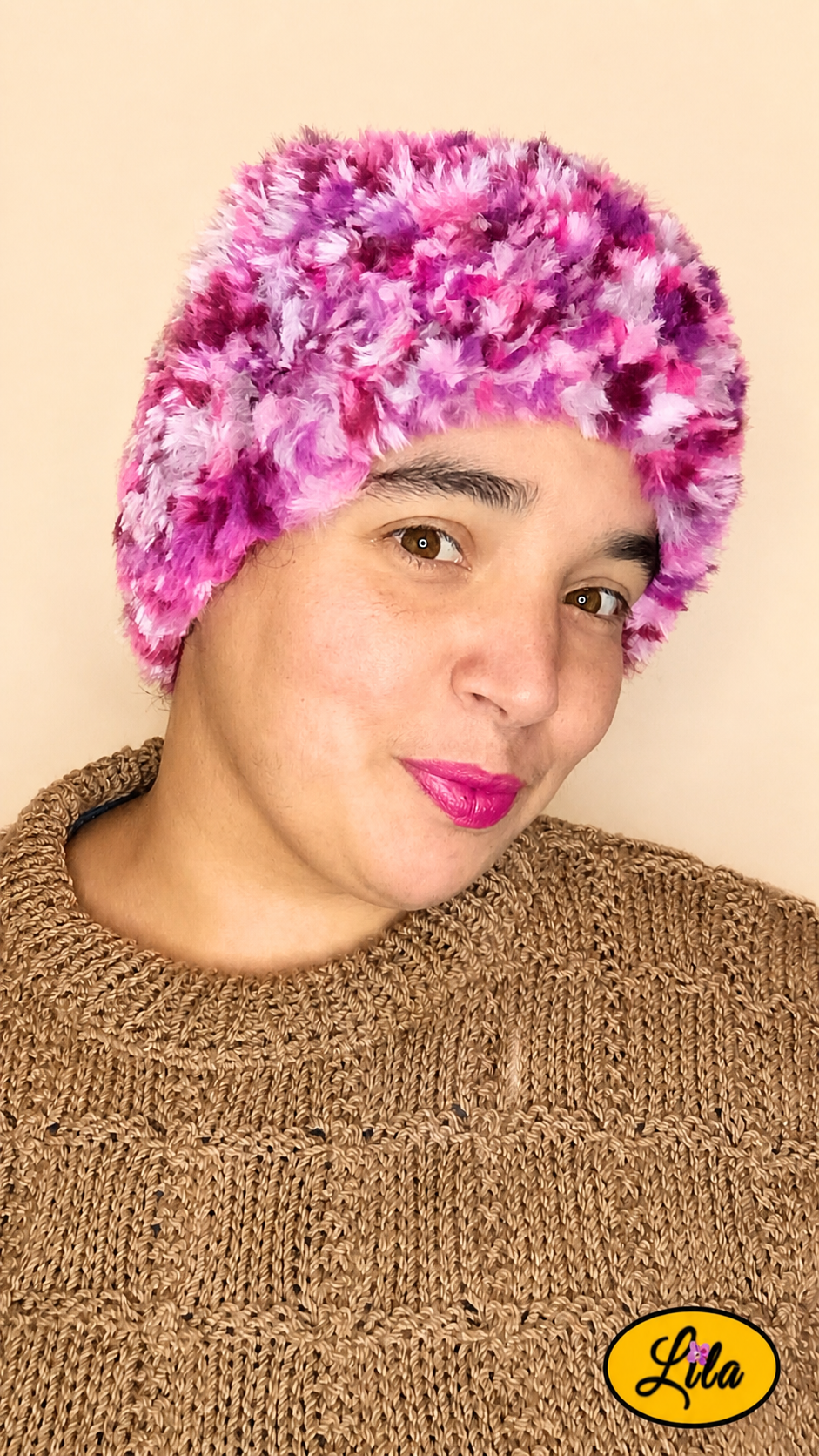 Cache-cou tricoté main rose chamarré effet fausse fourrure porté sur la tête par une femme avec pull brun sur fond crème vue de face légèrement orientée vers le profil droit style hivernal et tendance
