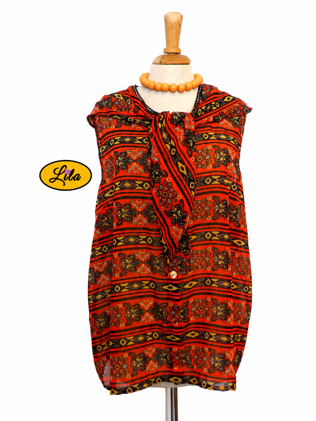 Chemisier Delphine sans manches en tissu léger orange et noir légèrement transparent porté sur mannequin de couture avec col noué sur fond blanc style rétro chic et élégant