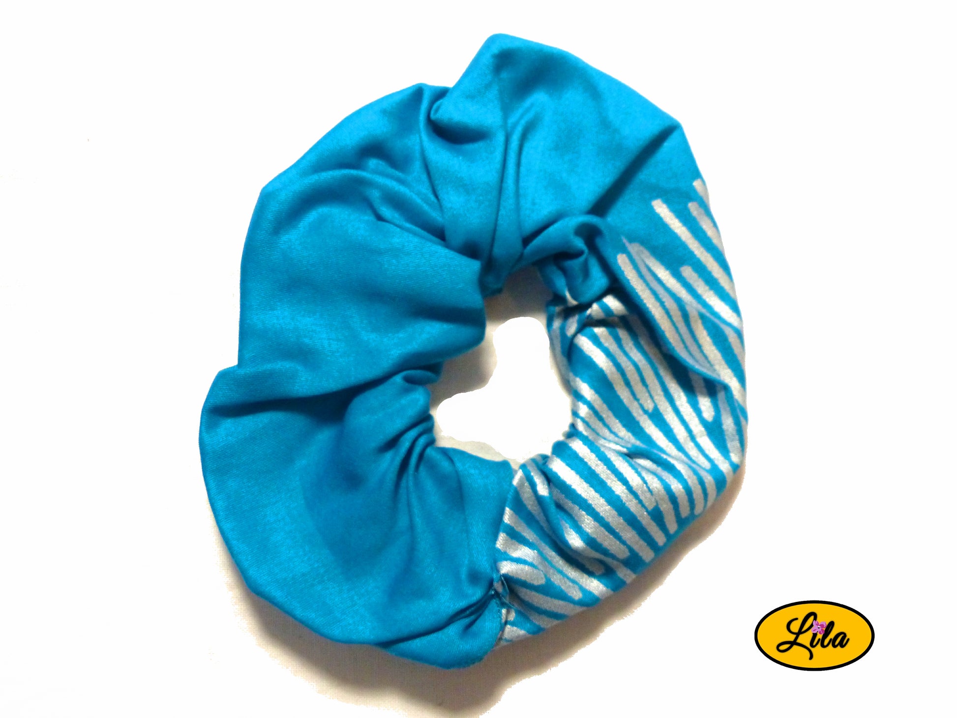 Chouchou pour cheveux en tissu turquoise avec quelques lignes argentées visibles sur le bas droit présenté sur fond blanc style moderne et artisanal