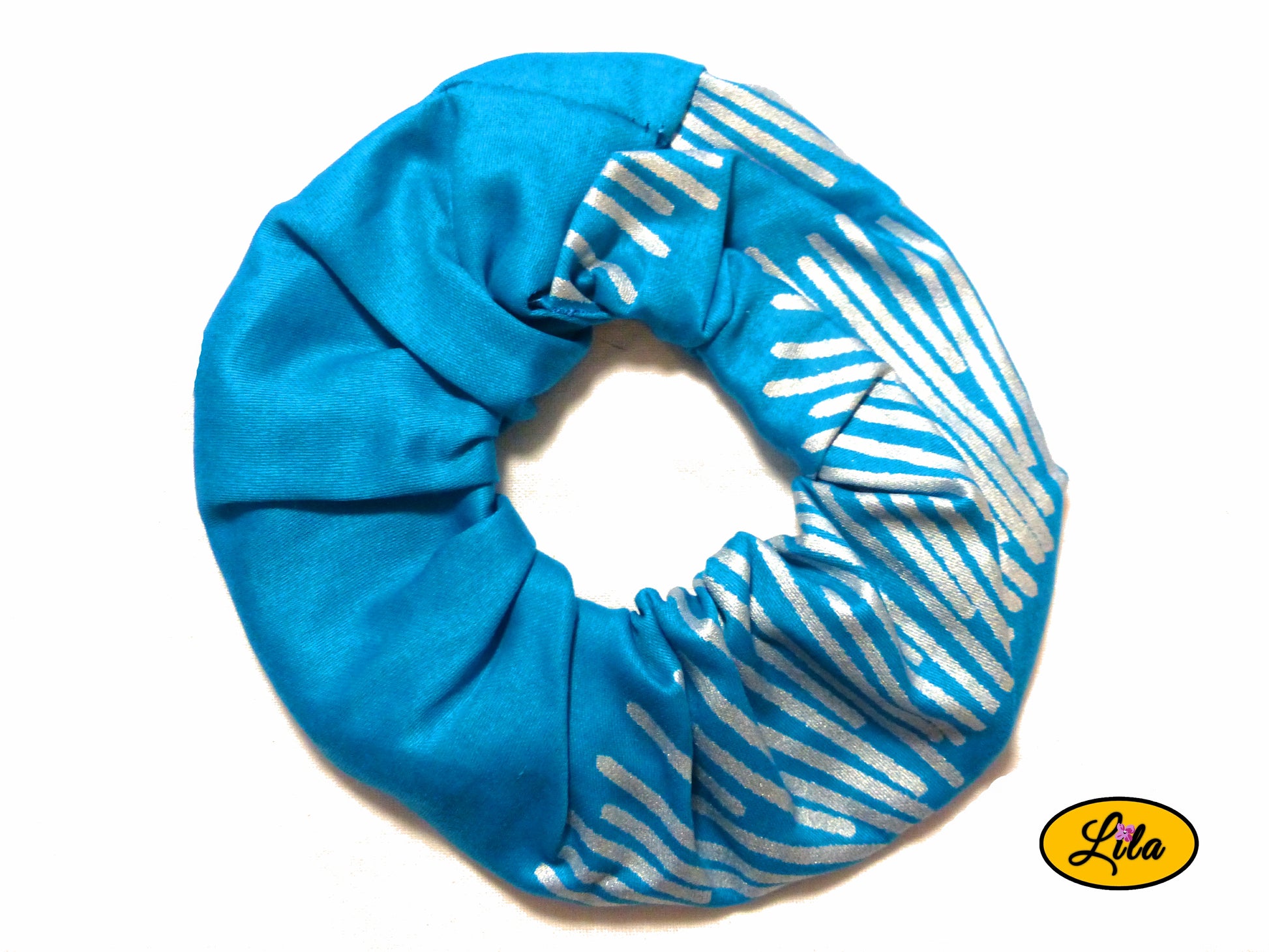 Chouchou pour cheveux en tissu turquoise avec motifs de lignes argentées couvrant la moitié droite du chouchou présenté sur fond blanc style lumineux et artisanal