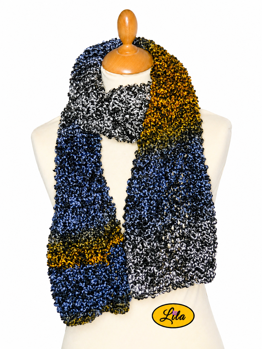 Écharpe crochetée multicolore tricotée à la main aux tons noir blanc bleu et orange enroulée autour d’un mannequin de couture avec côtés pendants sur fond blanc style cocooning et créateur