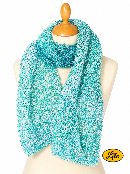 Écharpe crochetée verte tricotée à la main avec dégradés de vert enroulée autour d’un mannequin de couture avec côtés pendants sur fond blanc style cocooning et artisanal