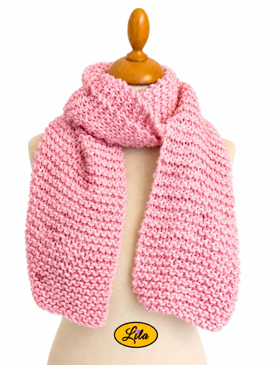 Écharpe rose tricotée à la main enroulée autour d’un mannequin de couture avec les côtés pendants sur fond blanc style chic et cocooning