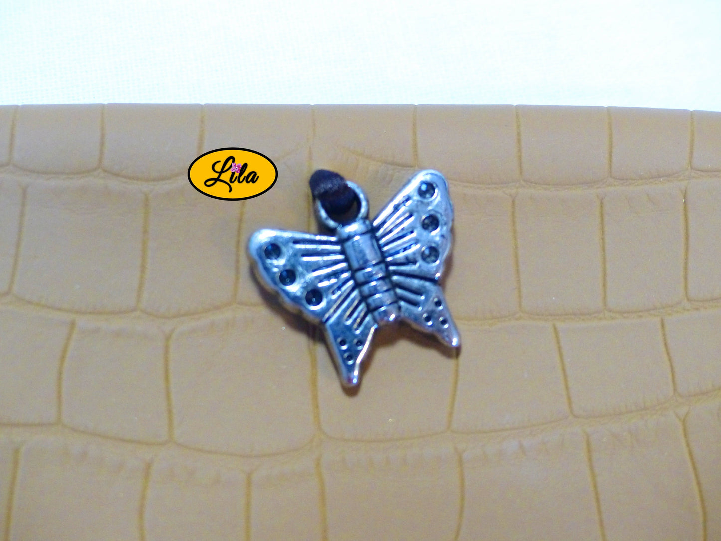 Zoom sur le pendentif papillon argenté décoratif de l’étui à lunettes en simili brun craquelé détail vintage et féminin