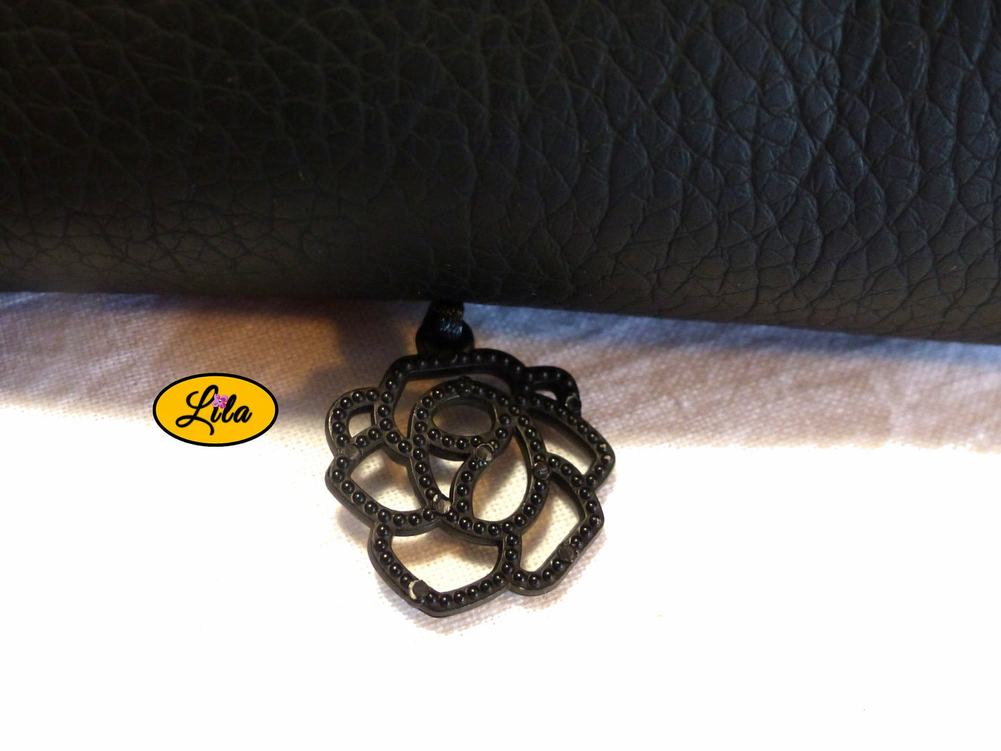 Zoom sur le pendentif noir en plastique dur représentant une fleur stylisée décorant l’étui à lunettes en simili noir détail moderne et féminin